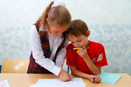 little girl and boy doing schoolwork; brother and sister doing their homework; sister helping brother with homework